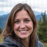 Close-up portrait of Elara Vance, a strong, smiling female adventure guide in her 30s with outdoor gear